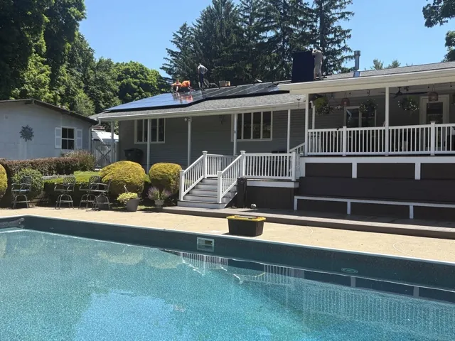 Installers placing black solar panels on a residential roof above a backyard pool