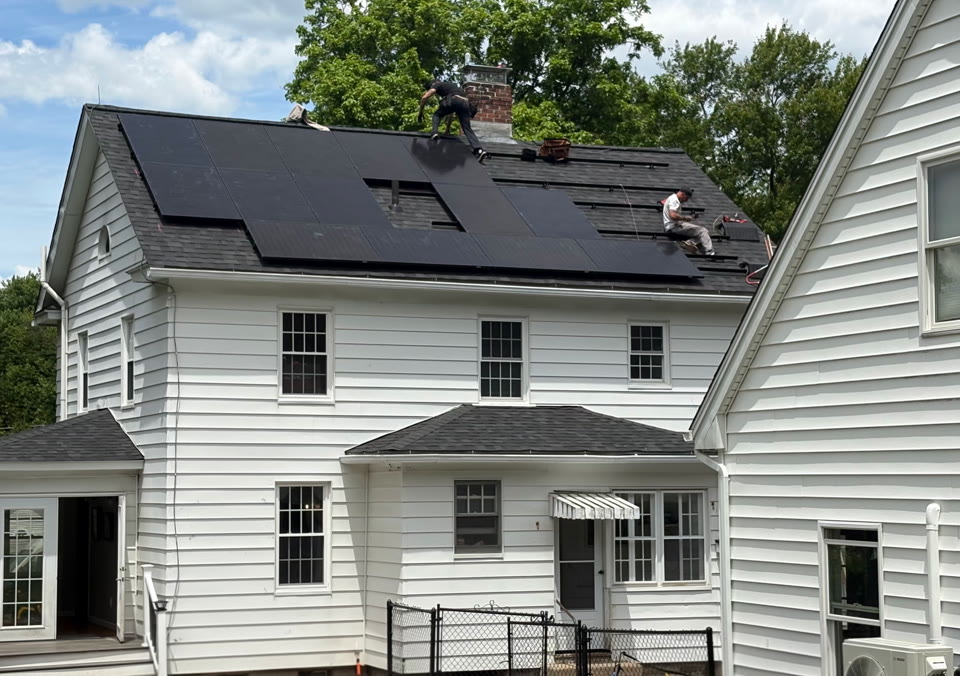 Installers working on black solar panels on a white residential home's roof