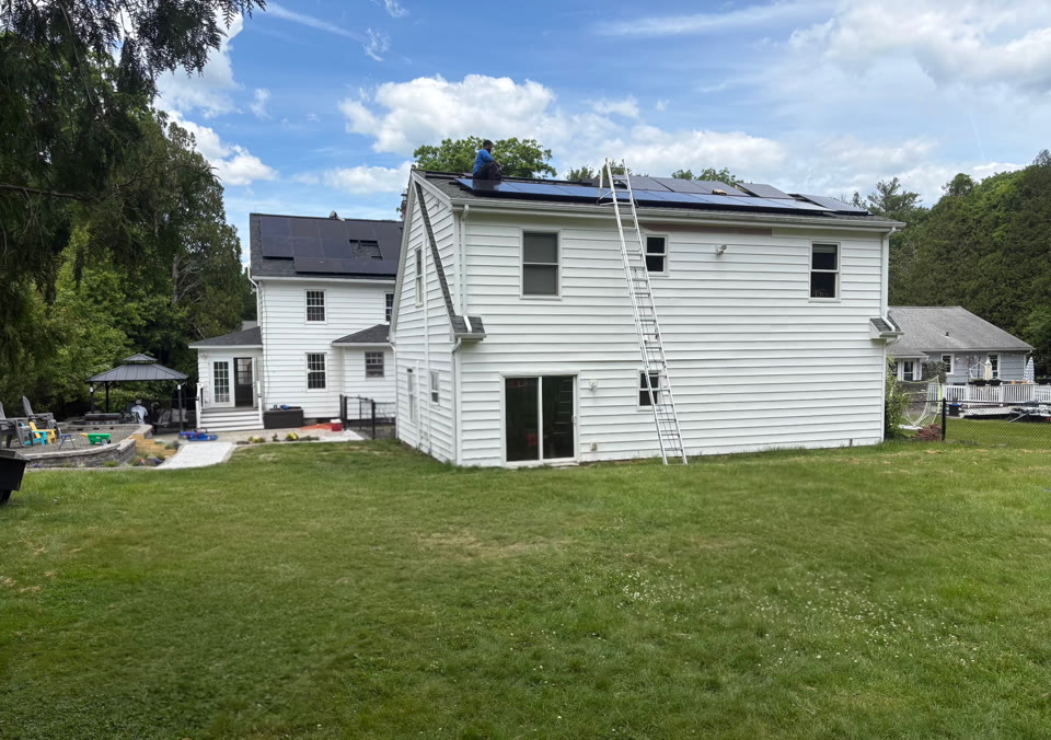 White residential home with rooftop solar panels, a ladder, and an installer on the roof
